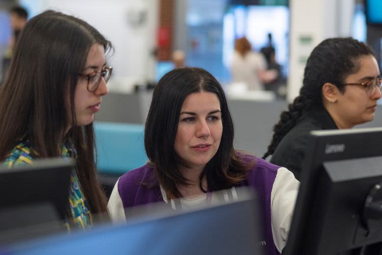 Customer services staff member looks at a PC monitor with a student
