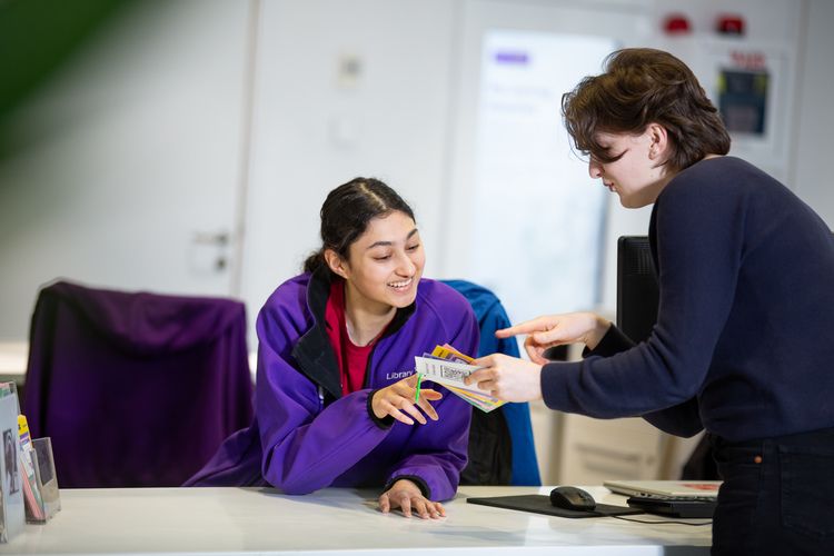 A student speaking to a staff member behind the customer service desk