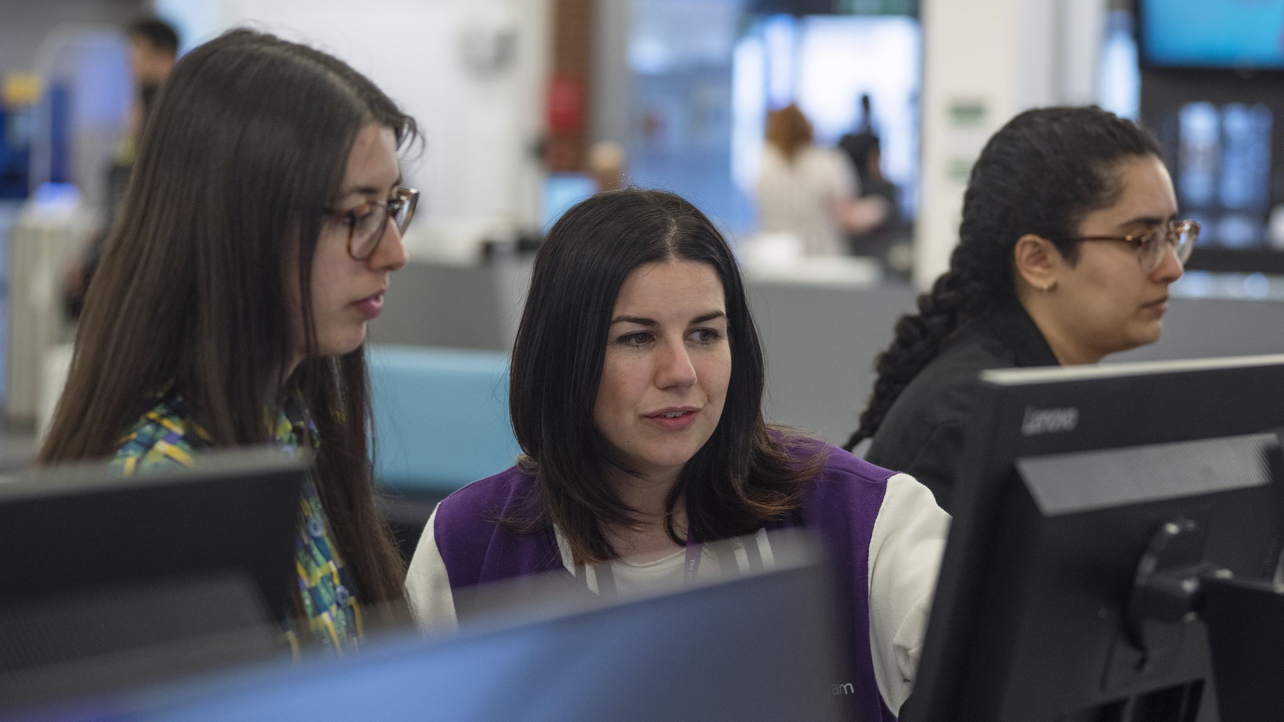 Library staff member pointing to a screen at PC cluster with a student