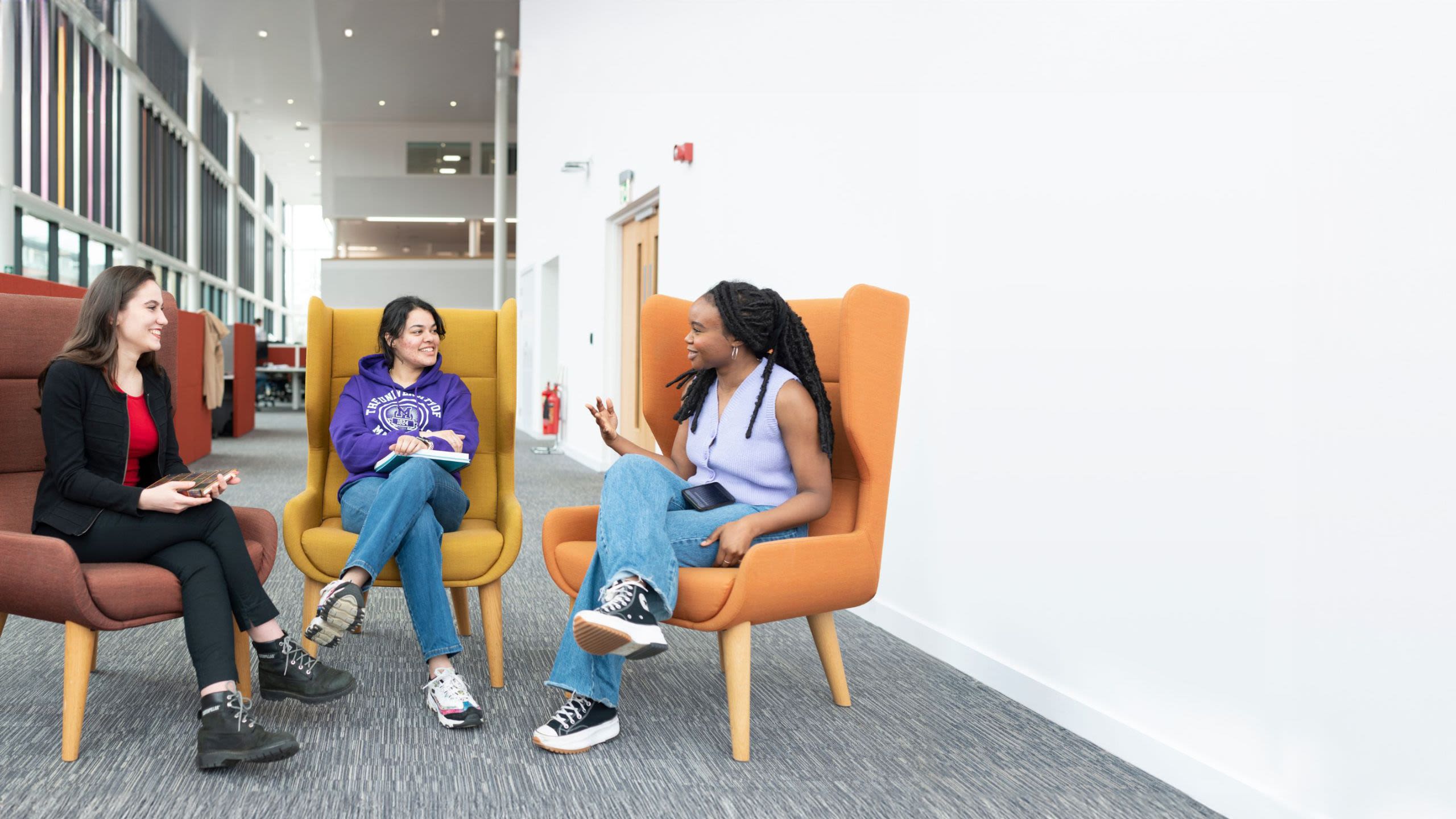 Students working in a study room in Green 2 in Main Library, while two students chat outside in the corridor