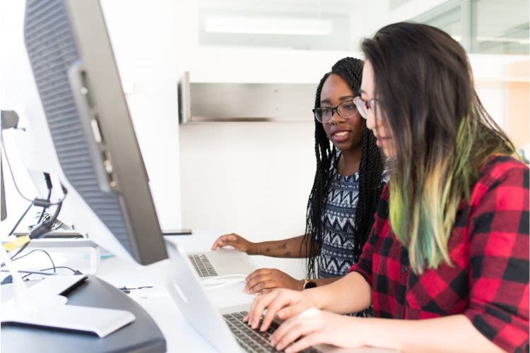 Two researchers typing on a keyboard as they work together in front of a desktop PC.