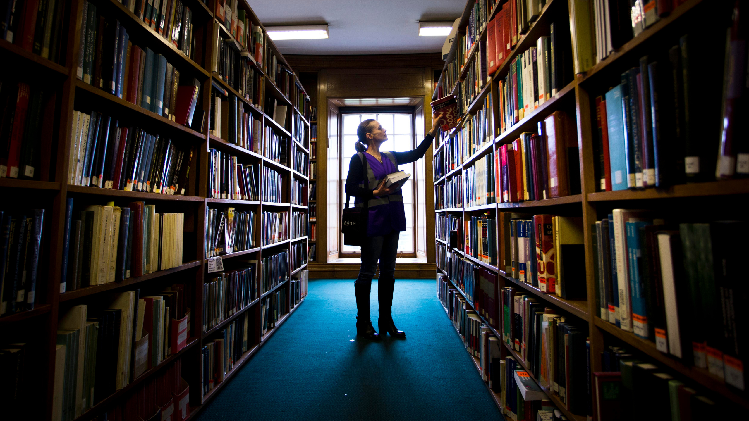 Woman reaching for a book off shelf in an aisle of Main Library