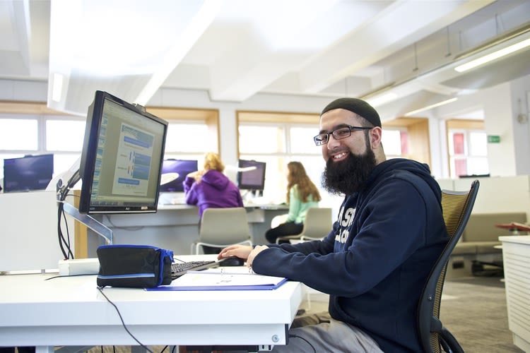A student smiling while working at a desktop PC in an AGLC PC cluster.