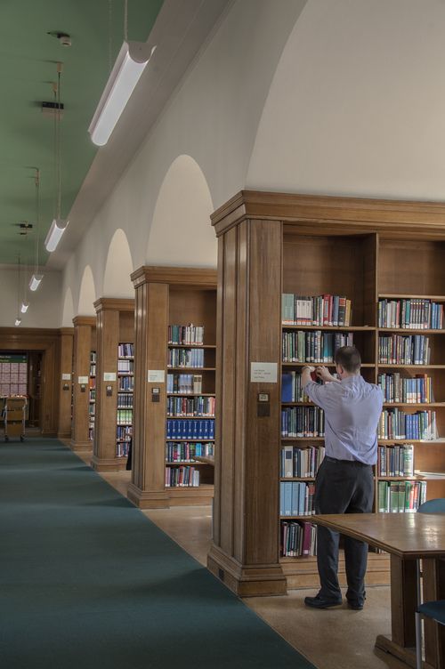 A staff member examining books on the shelves in Green 3 in Main Library