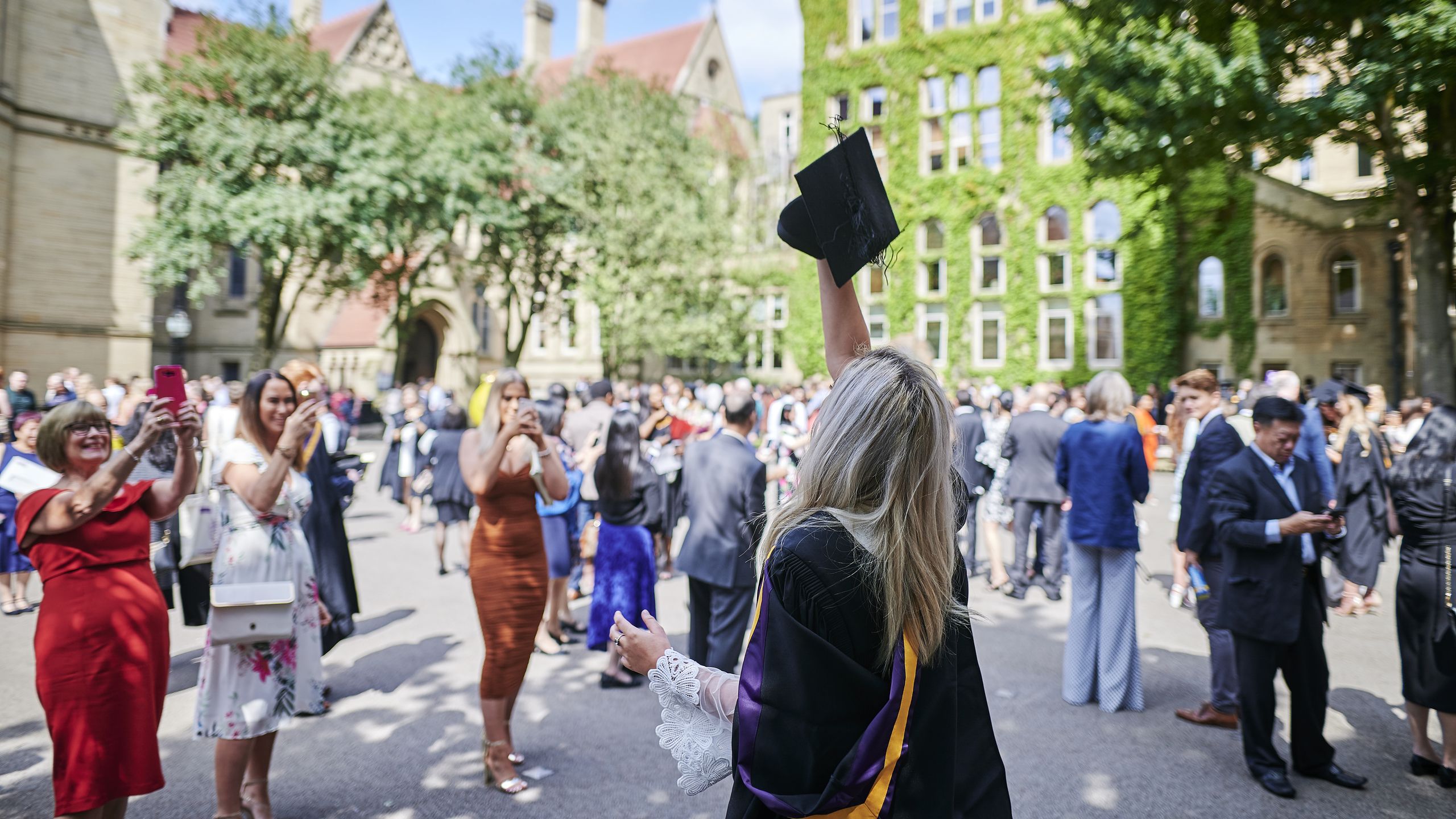 A student throwing mortar board in graduation gown in old quadrangle