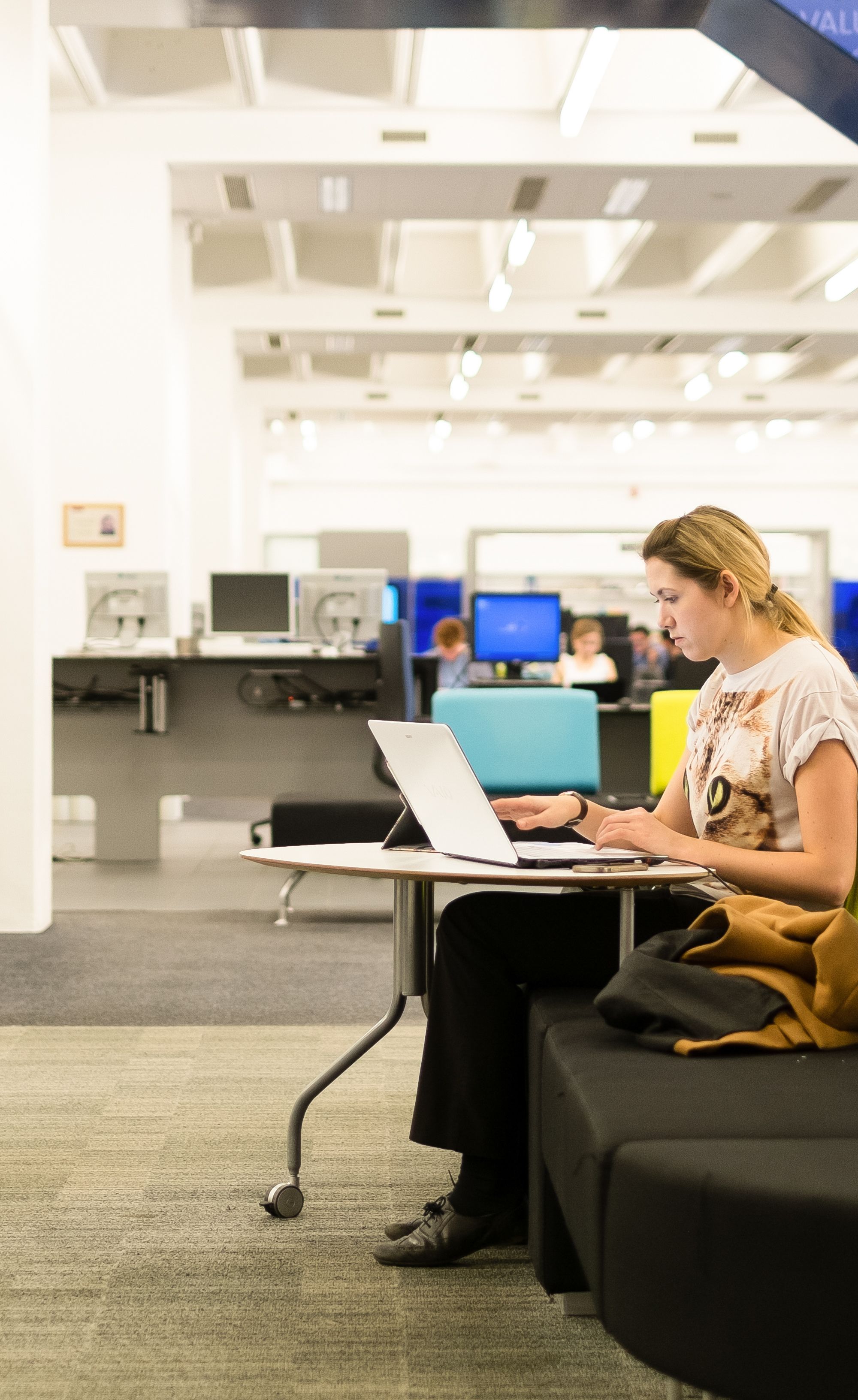Student in Blue Ground in Main Library looking at laptop on seat