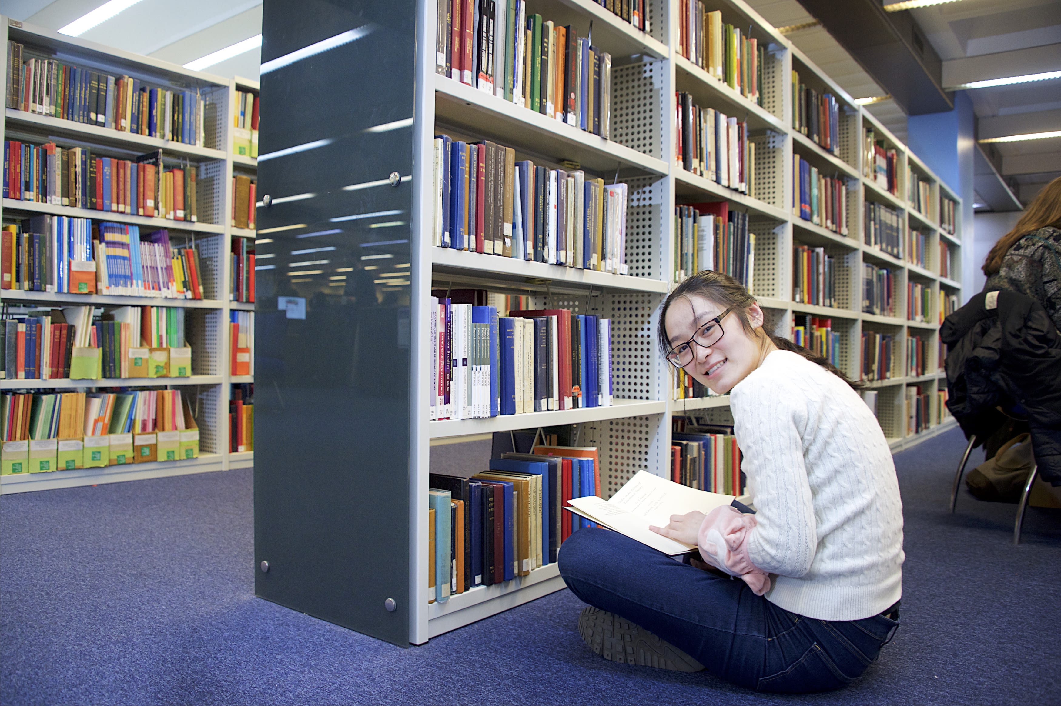 A student sitting down on the floor reading a book in the Library