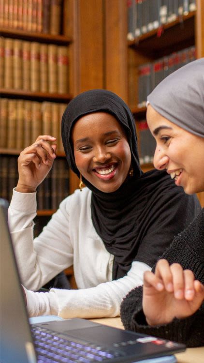 Student smiling in Main Library while looking at laptop
