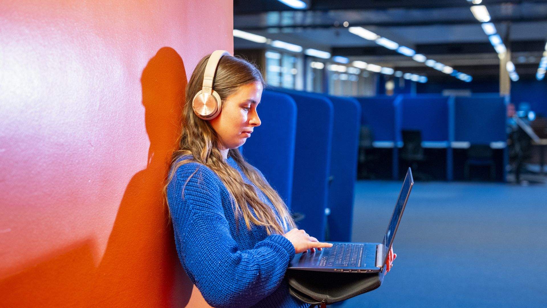 Student on laptop leaning against a wall in Blue 1