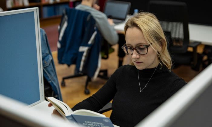 A woman reading a book at a desk in a Library building