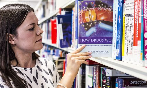 Woman pulling a book from a shelf titled 'How Drugs Work'