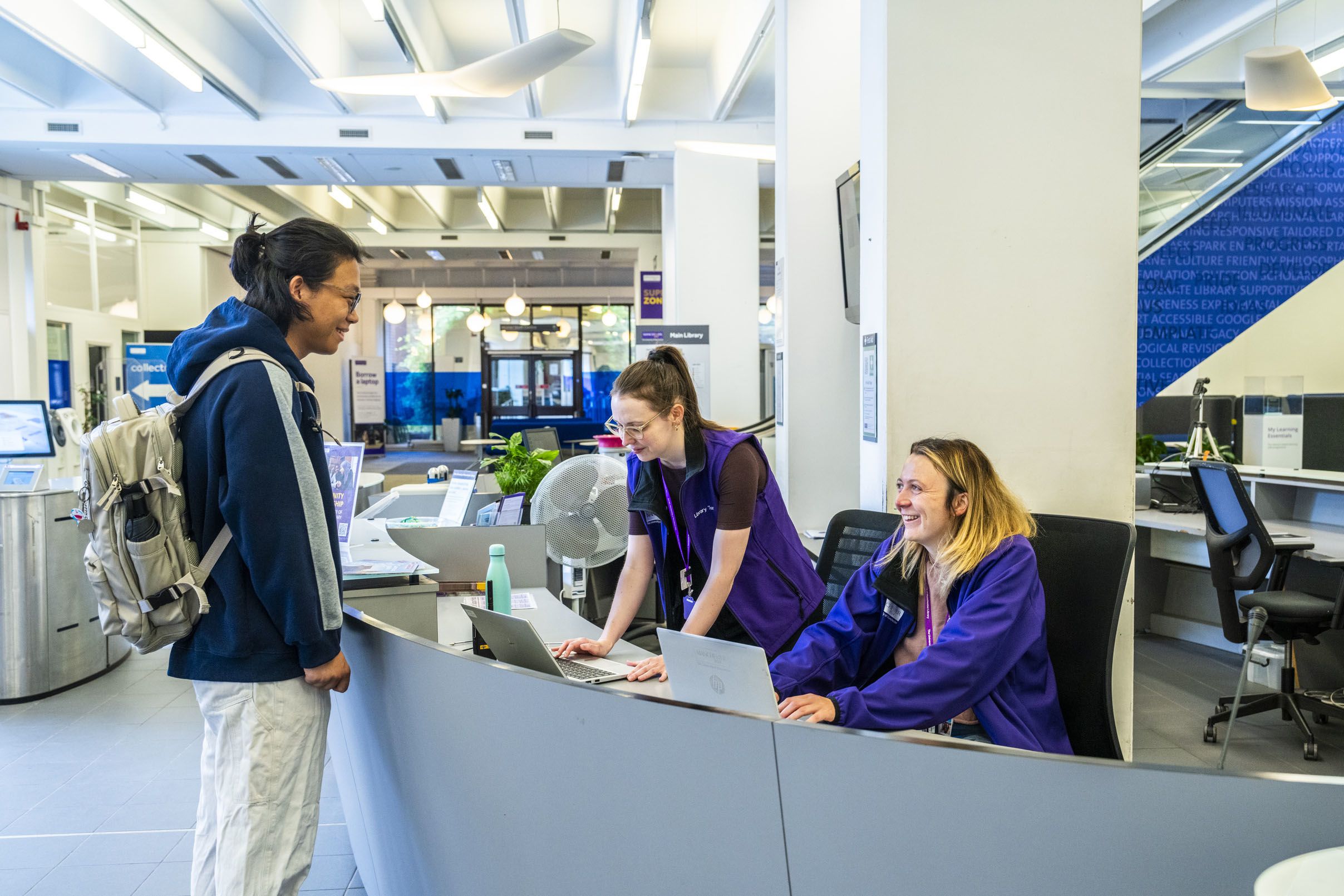 Student smiling while chatting to Library staff behind service desk in Main Library