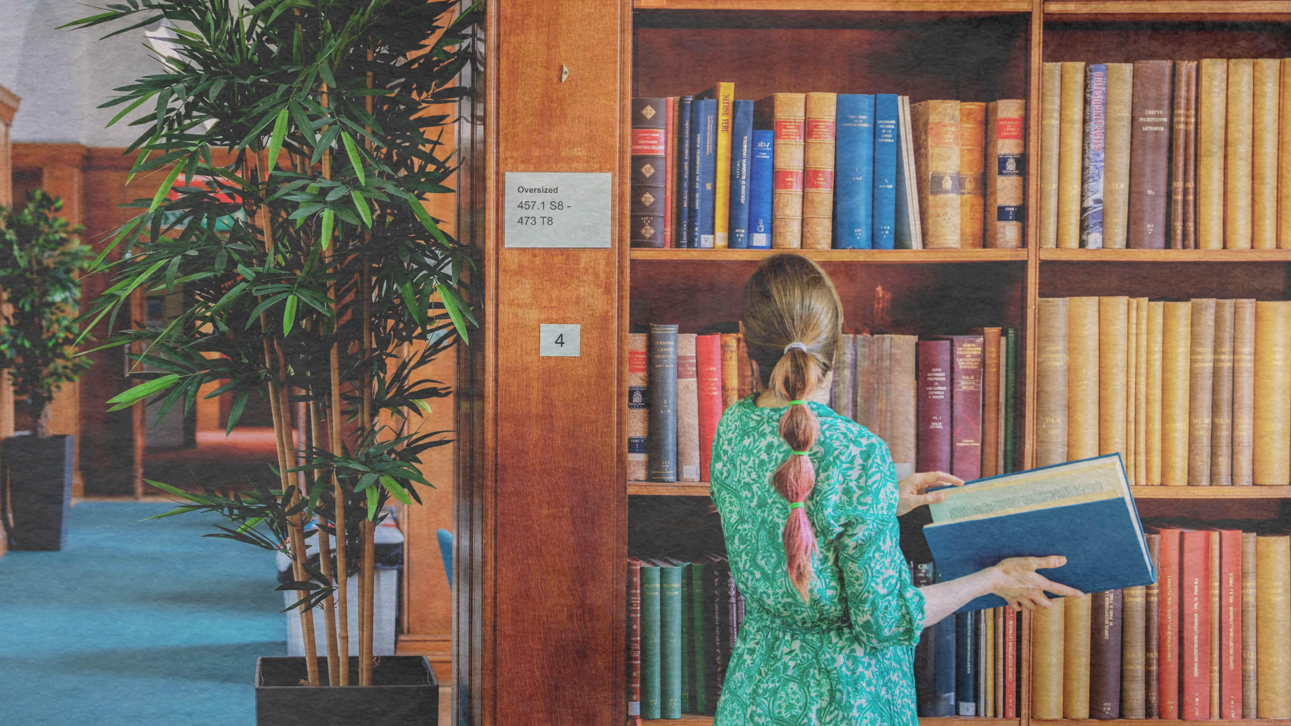 A woman looking at a book in a library standing by book shelves