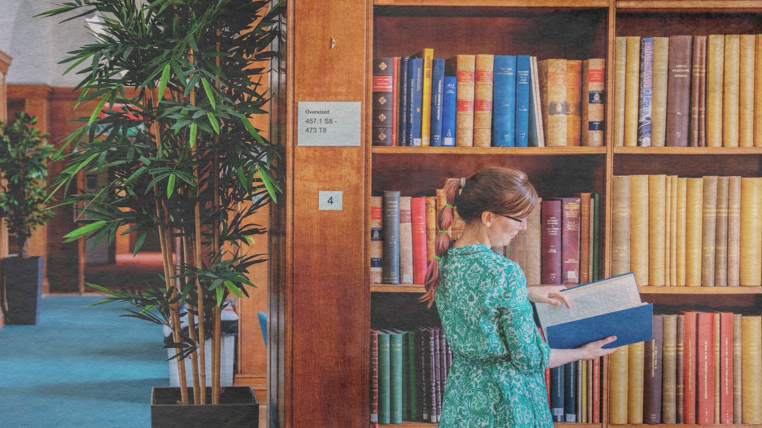 A woman looking at a book in a library standing by book shelves