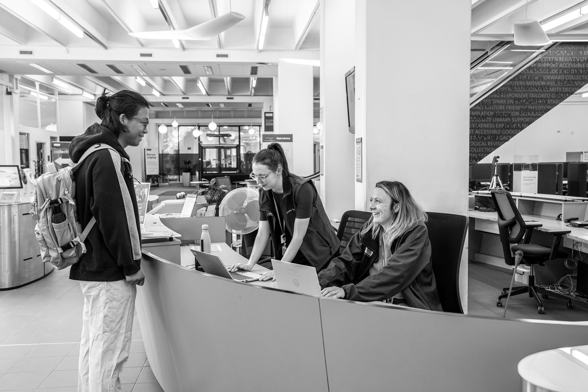 Student smiling with Library staff behind service desk in Main Library