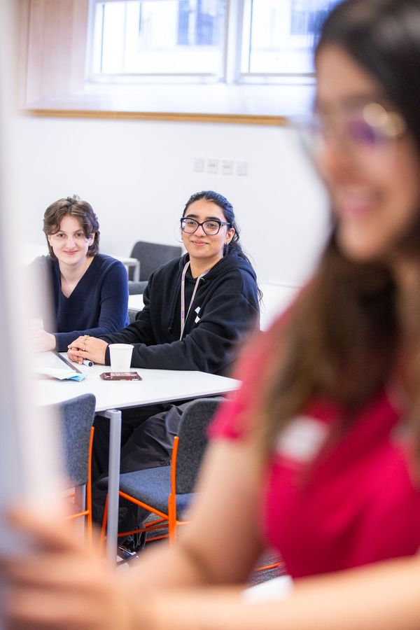 Two students sat in a workshop while a student team member is in foreground writing on a board
