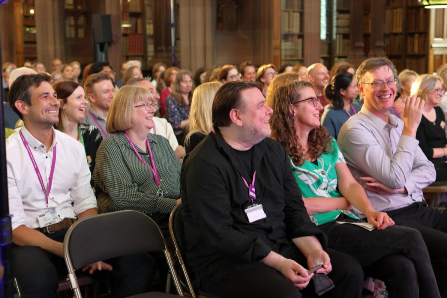 Staff smiling while sat in the plenary session which took place in the reading room at Rylands