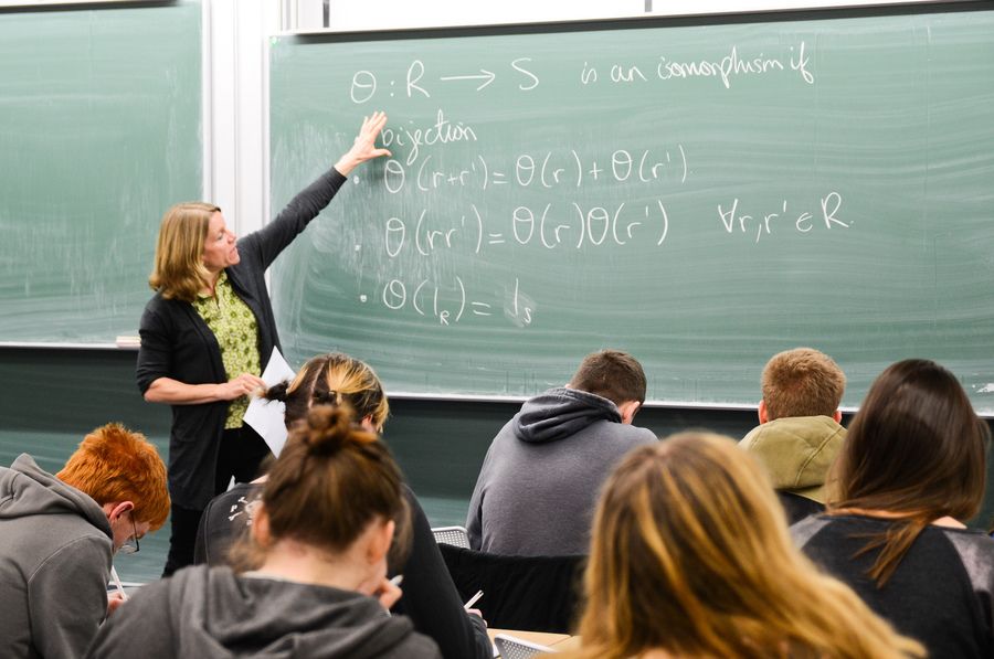 A female lecturer in front of a class gesturing at a blackboard