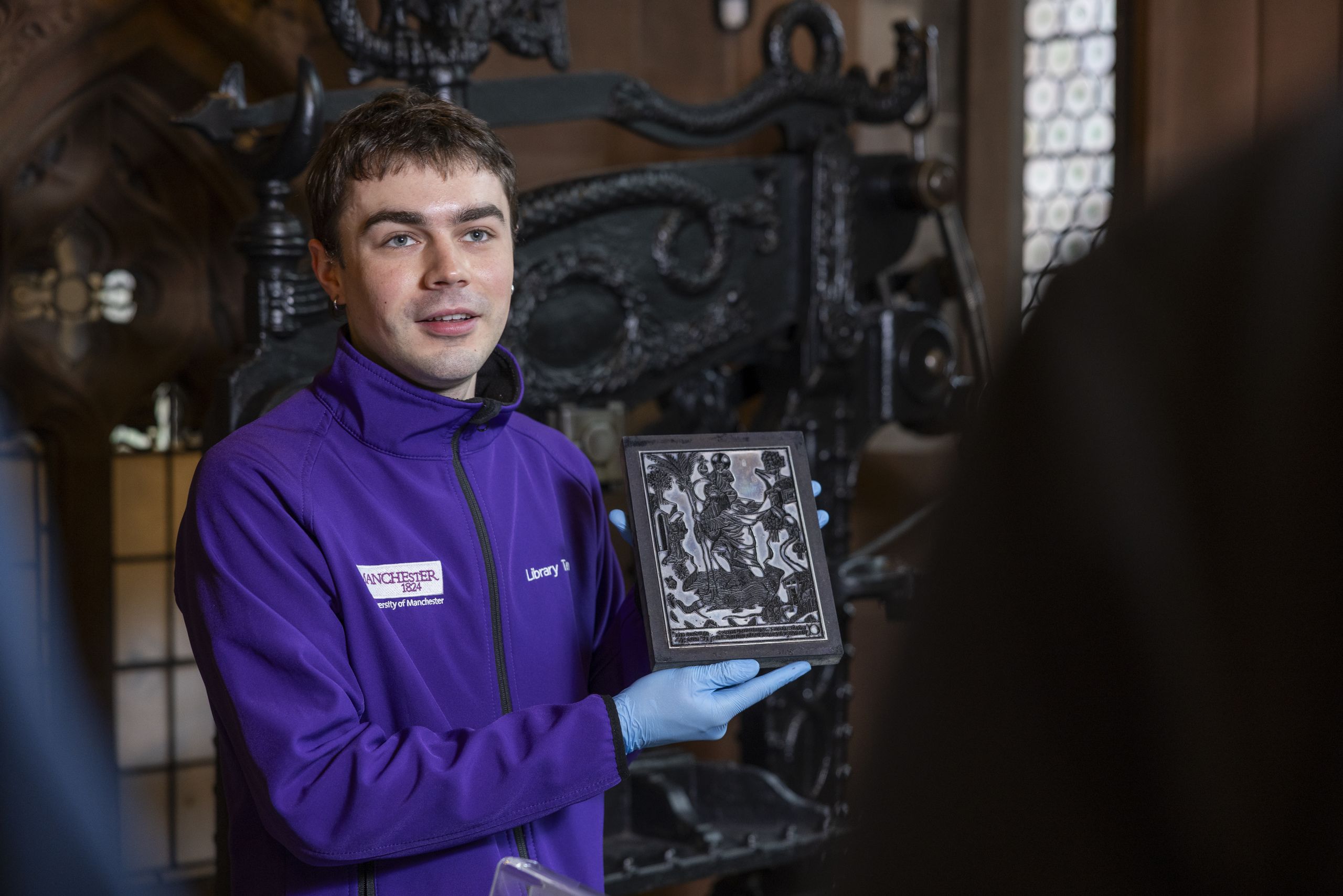 Member of Rylands staff holding an item from collections in front of printing press