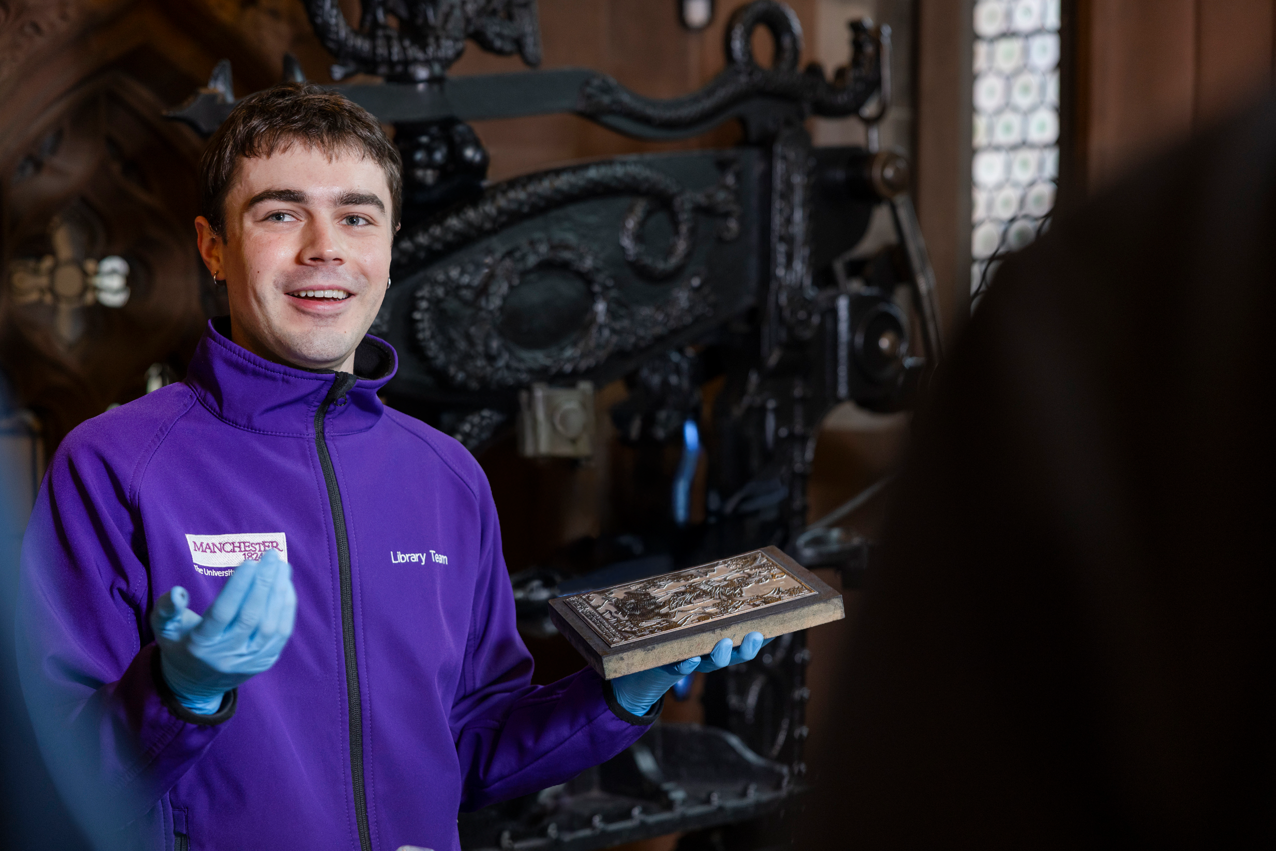 Member of Rylands staff holding an item from collections in front of printing press