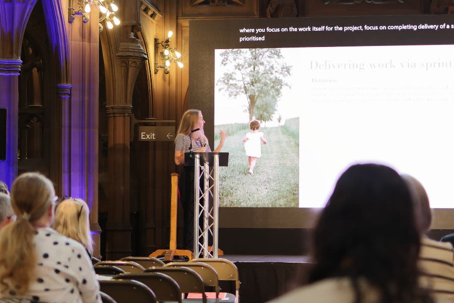 A woman presenting at the John Rylands Library in front of a screen with Powerpoint presentation shown