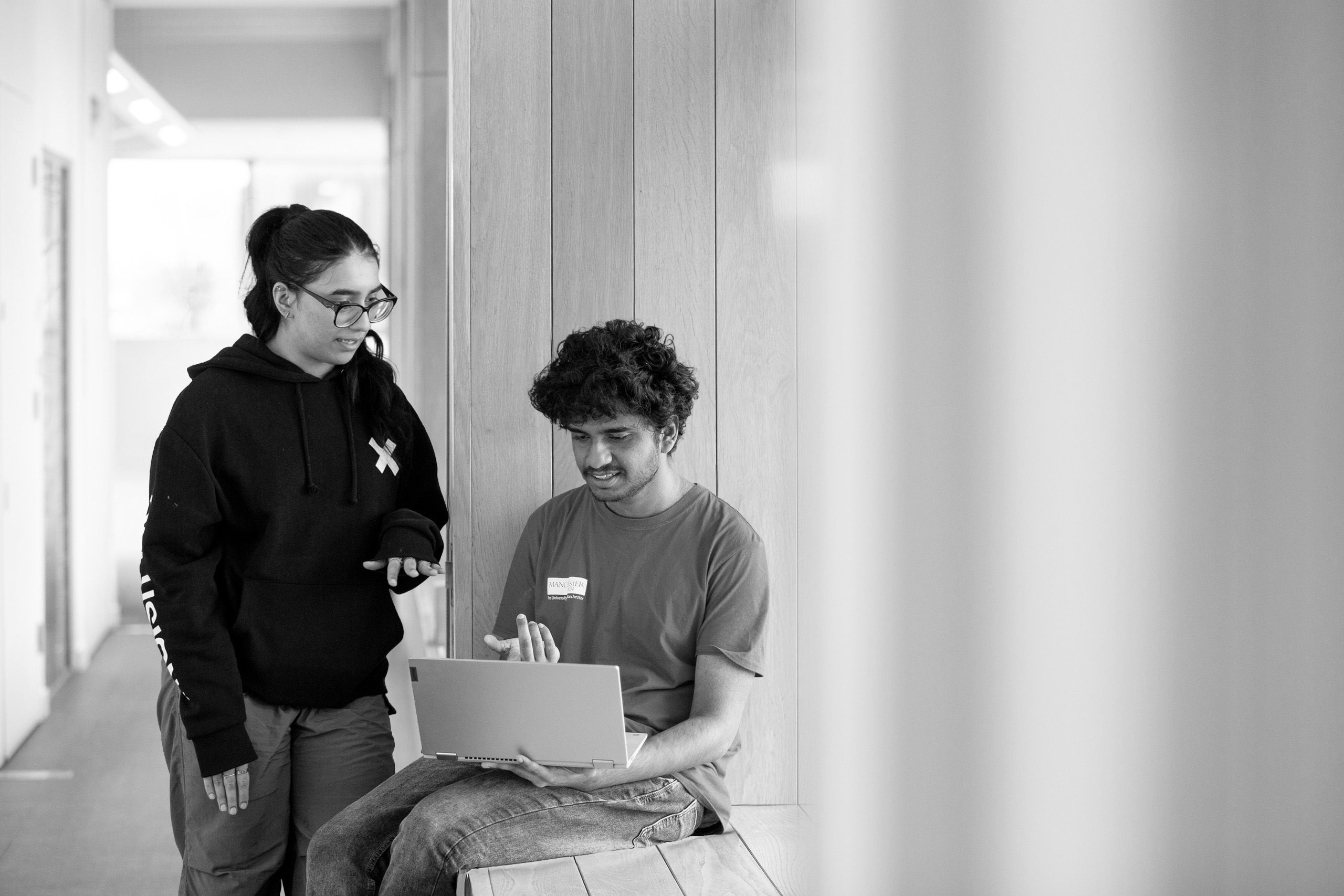Two students sat on a window ledge at AGLC looking at a laptop