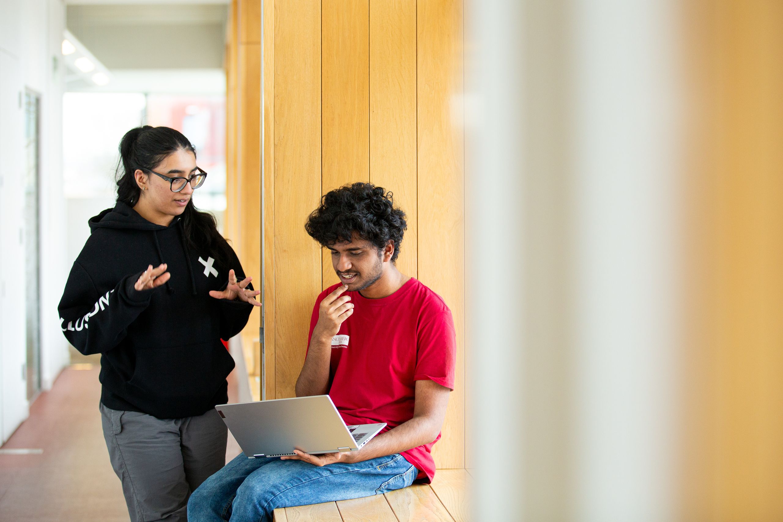 Two students looking at a laptop while sat on a window ledge in AGLC