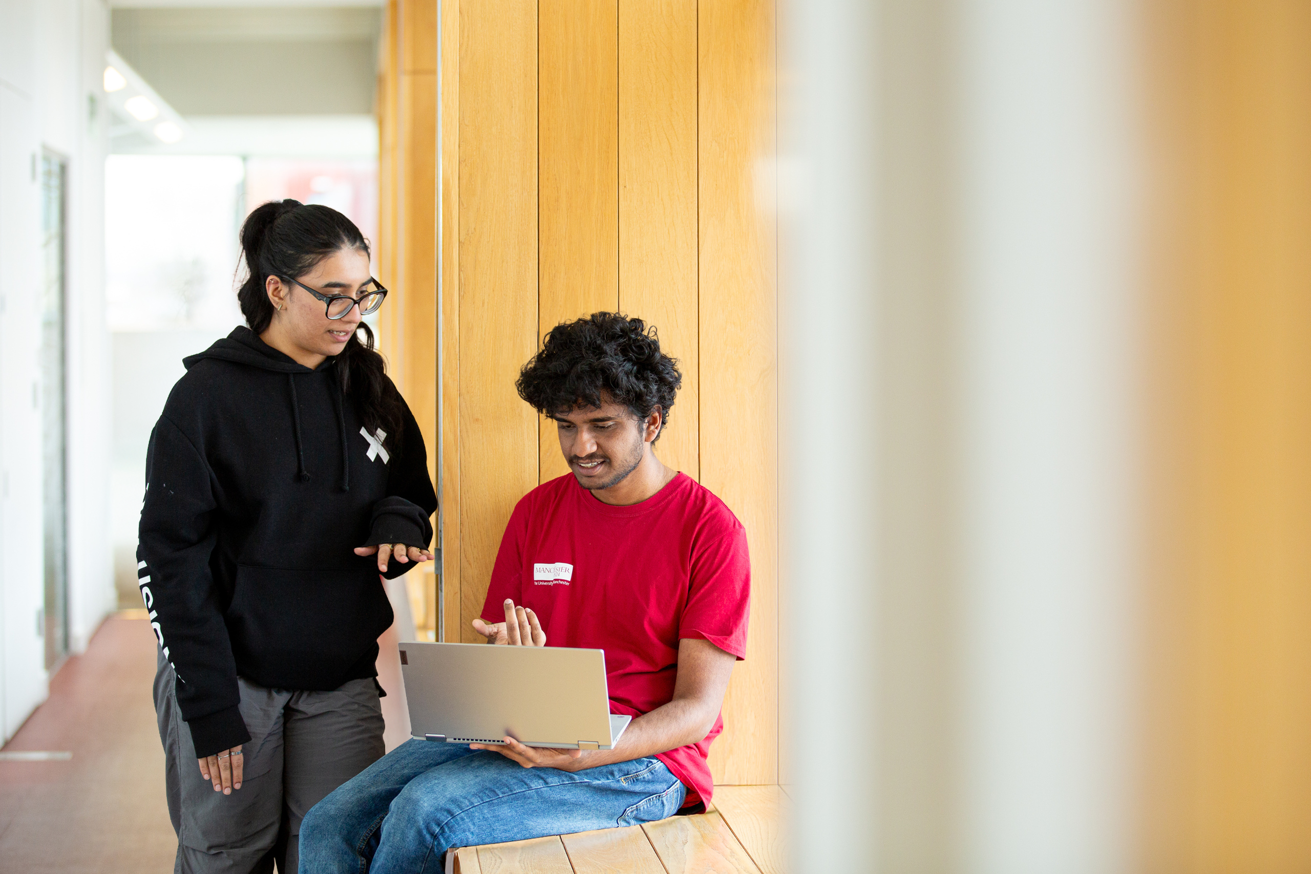 Two students sat on a window ledge while looking at a laptop in AGLC