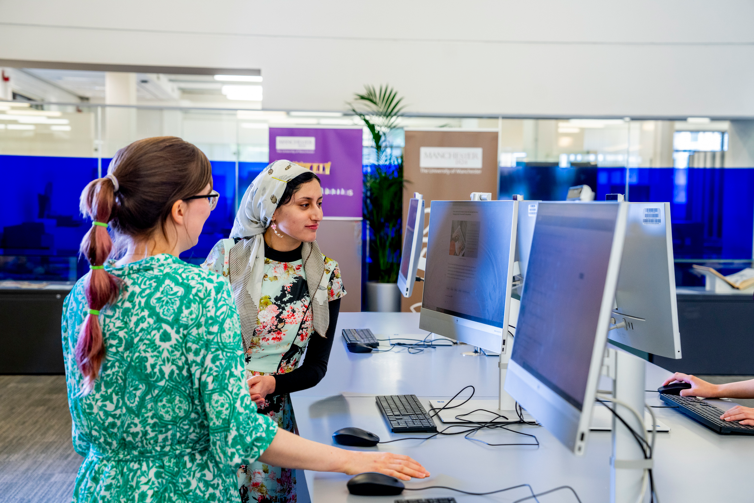 Two students speaking while standing at quick use PCs in Blue Ground Main Library