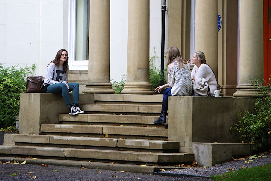 Three students sat on steps outside a building in conversation