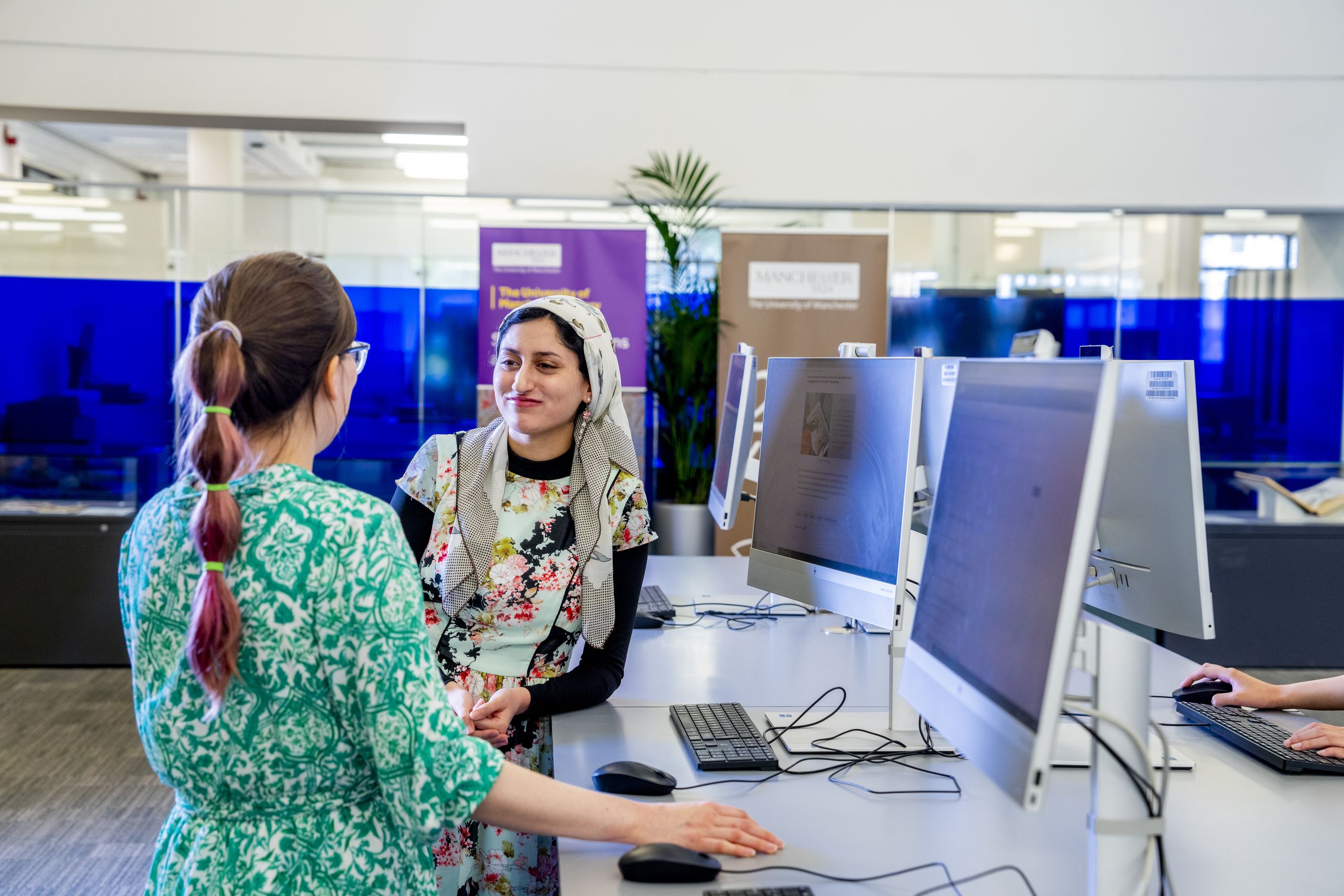 Two students speaking while standing at quick use PCs in Blue Ground Main Library